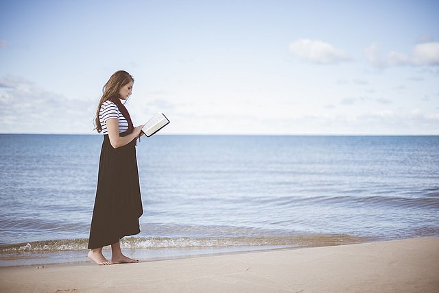 Eine junge Frau liest am Strand von Föhr.
