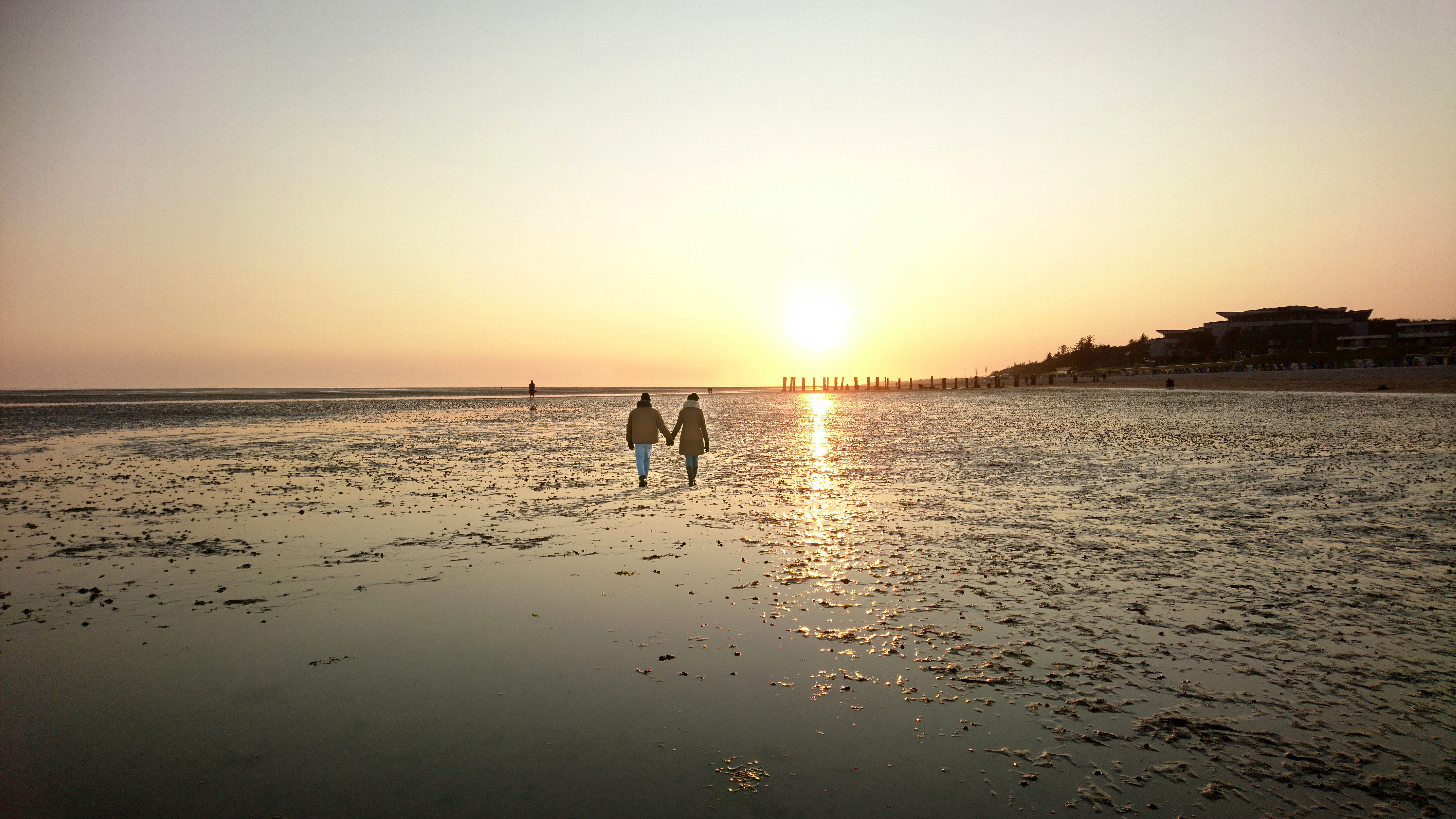 Urlauber laufen Hand in Hand im Watt in den Sonnenuntergang.