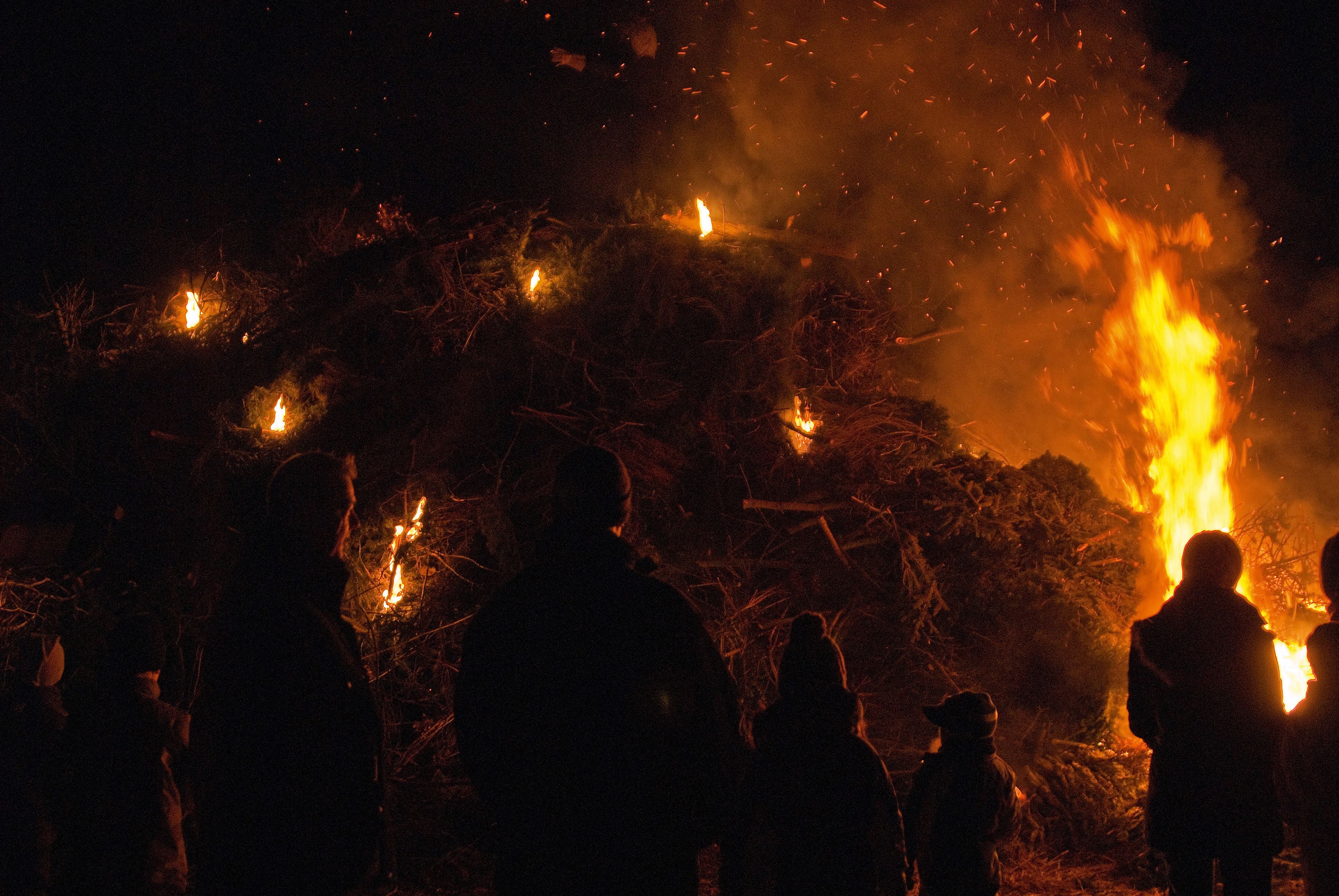 Großes Biikefeuer auf der Insel Föhr bei Nacht mit Menschen im Feuerschein