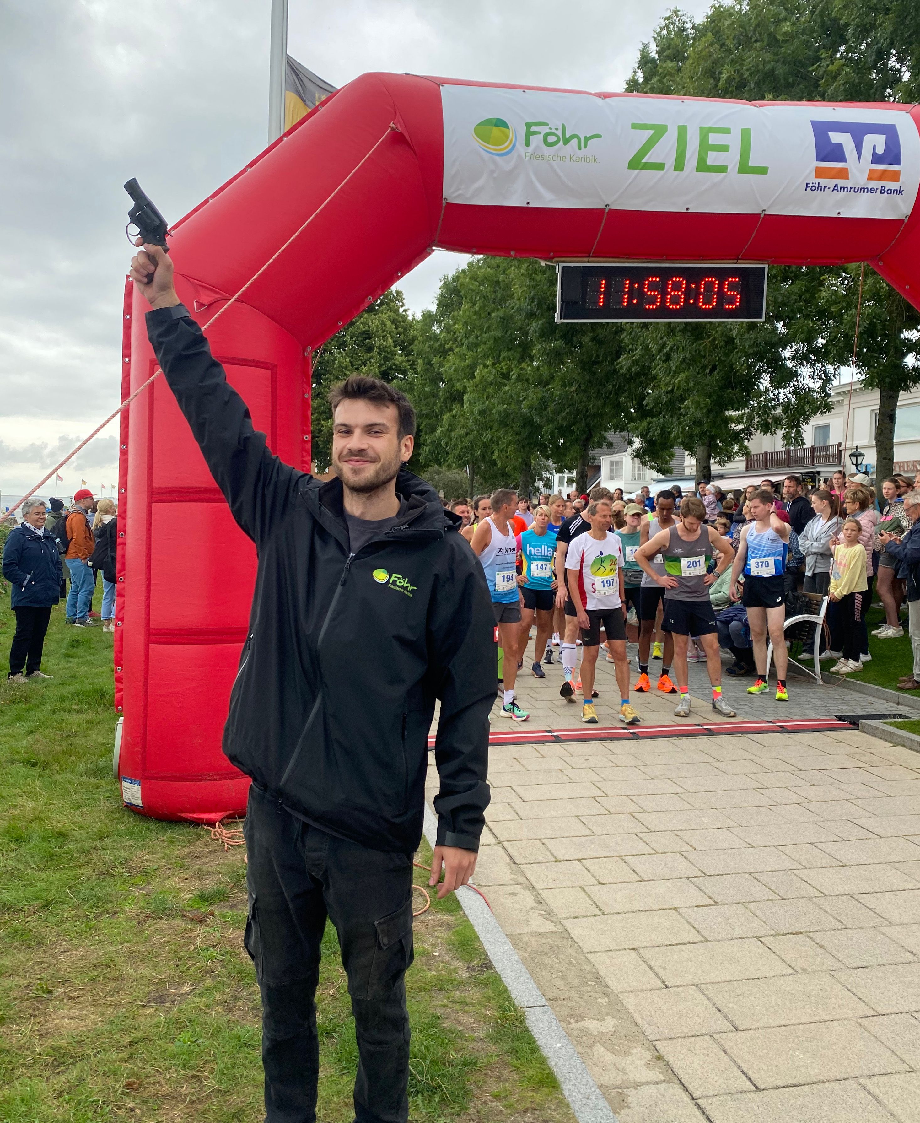 Junger Mann mit Startpistole vor Lauf-Startbogen