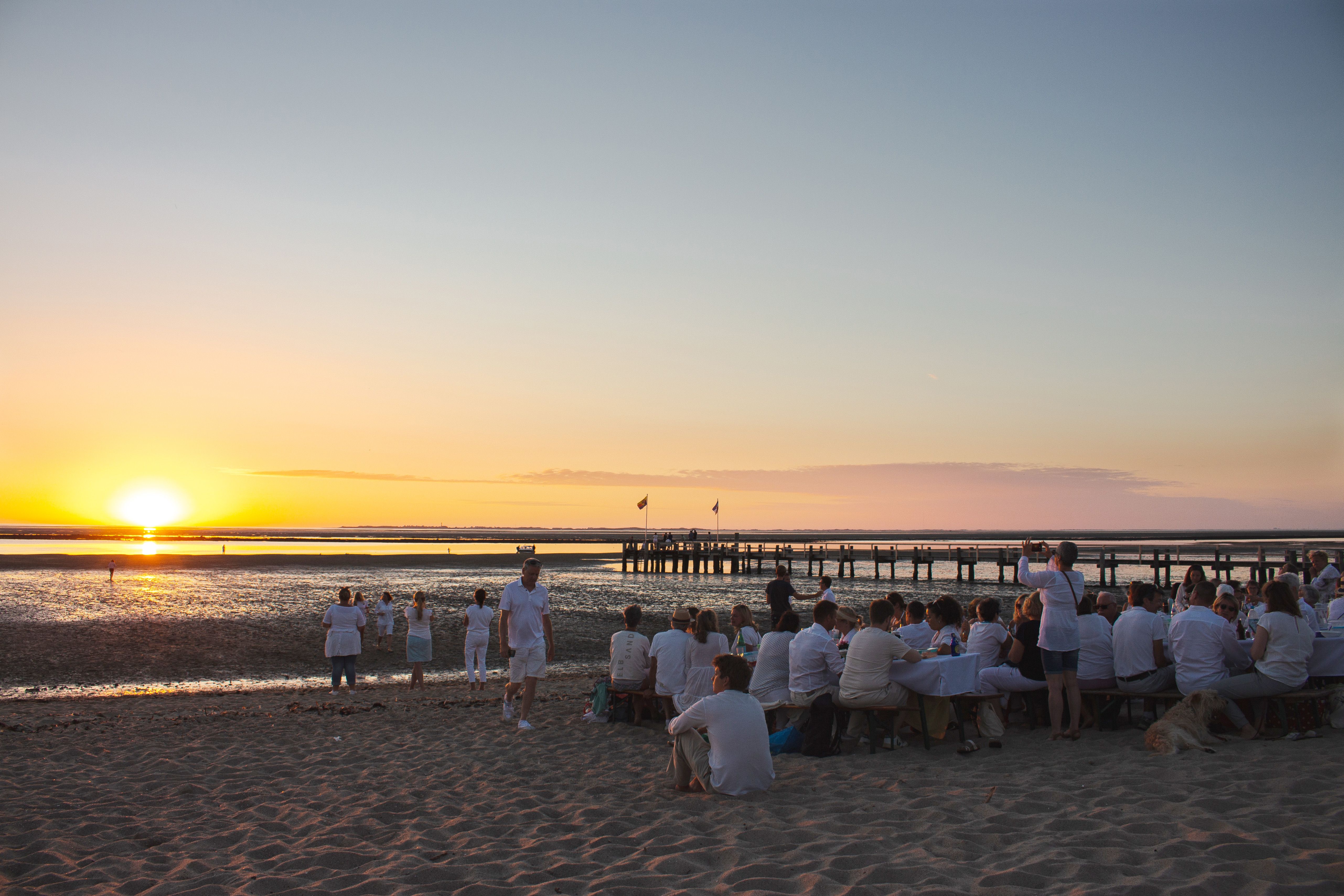 Teilnehmnde des White Dinners am Utersumer Strand auf der Nordseeinsel Föhr genießen den Sonnenuntergang ganz in weiß gekleidet.