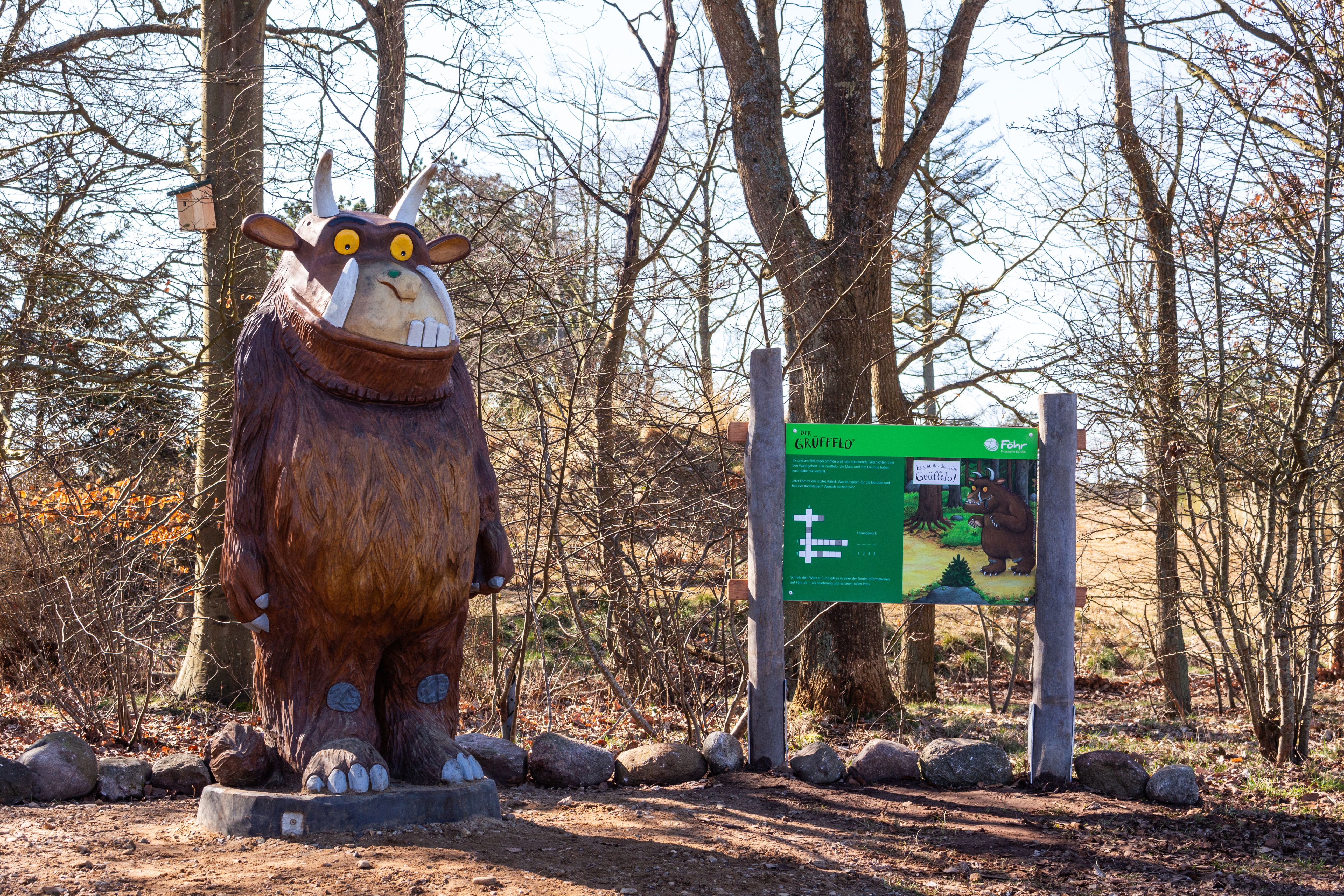 Grüffelo-Figur im Wald neben einem Hinweisschild