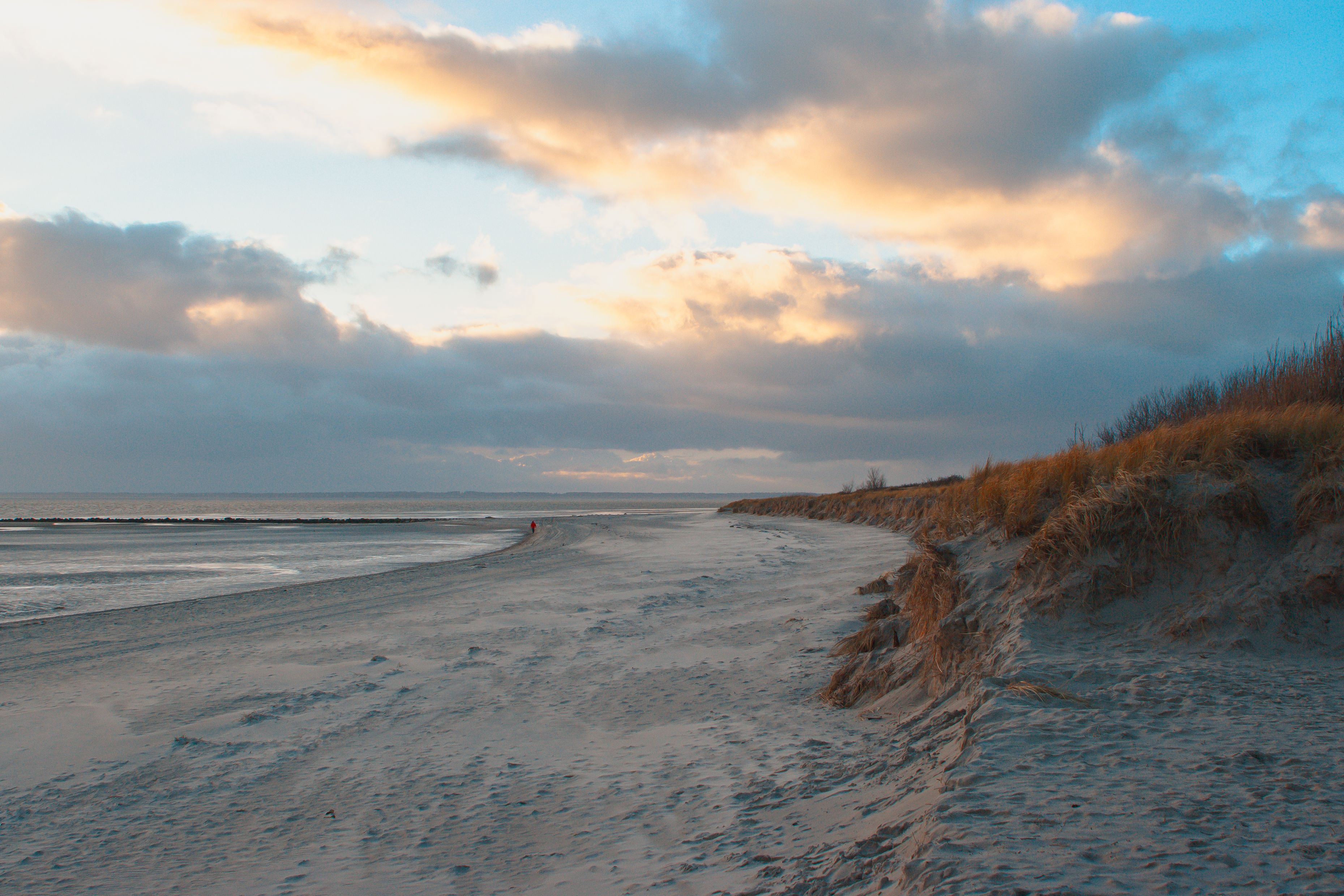 Nieblumer Strand zum Sonnenuntergang mit einer Spaziergängerin am Strand.