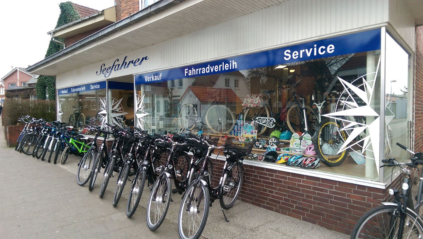 Fahrräder vor dem Seefahrer und ein Schaufenster mit Helmen, Rädern und vielem mehr von Fahrradverleih Seefahrer auf Föhr